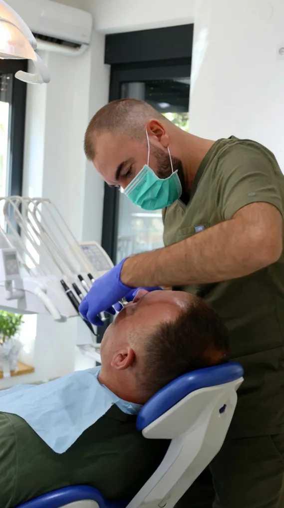Stomatolog sa maskom i rukavicama pregleda pacijenta u stomatološkoj stolici